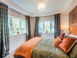 A bedroom with a bed orange and green bedding two windows with curtains and a ceiling light at Broadsands in Paignton