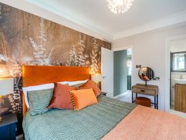 A bedroom with an orange headboard green bedding and decorative pillows along with a vanity and a view into a bathroom at Broadsands in Paignton