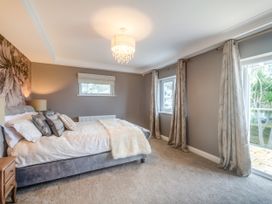 A bedroom with a bed, bedside table, window with curtains, and a chandelier at Broadsands in Paignton
