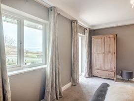 A bedroom with windows and curtains a wooden wardrobe and a small ottoman at Broadsands in Paignton