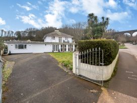 A driveway leading to a two-story white house with a balcony and a garage behind a metal gate at Broadsands in Paignton