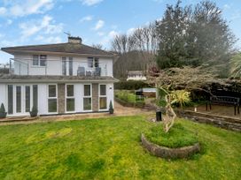 A two story house with glass balcony and garden with tree and benches at Broadsands in Paignton