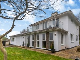 A two story house with white exterior walls windows and a balcony surrounded by grass and trees at Broadsands in Paignton