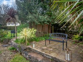 A garden patio with a black metal bench two lanterns with candles a wooden shed trees and plants at Broadsands in Paignton