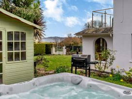 A garden with a hot tub a green shed a black barbecue grill and a white house with a glass balcony at Broadsands in Paignton