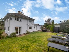 A two-story house with white walls and gray roof next to a garden with patio furniture and lounge chairs at Broadsands in Paignton
