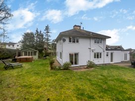A backyard with a two-story white house a green garden shed lounge chairs a hot tub and barbecue grill at Broadsands in Paignton