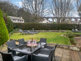 A garden with a glass table and chairs and sun loungers on a lawn with trees and houses in the background at Broadsands in Paignton