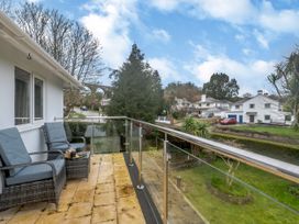 A balcony with two chairs and a small table overlooking a garden with houses and trees at Broadsands in Paignton