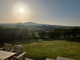 A garden with grass and wooden chairs and table with hills and sun in the background at Angorfa in Aberdaron