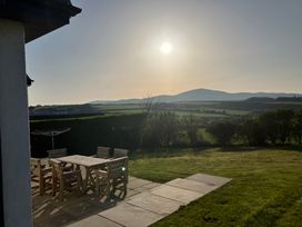A patio with a wooden table and six chairs overlooking a grassy yard and hills at Angorfa in Aberdaron