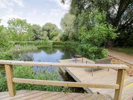 A pond with a wooden deck and a chair at The Shepherds Hut at Bridge Lake Farm & Fishery Chacombe