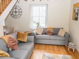 A living room with two grey sofas and cushions a wall clock and a window at 1 Greenswood Court in Brixham