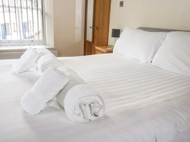 A bedroom with a bed made with white linens and towels on it next to a window and wooden door at 1 Greenswood Court in Brixham