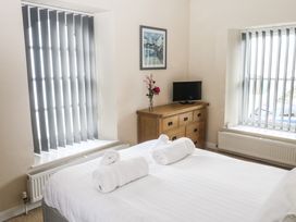 A bedroom with a bed with rolled towels a wooden dresser with a television and two windows with vertical blinds at 1 Greenswood Court in Brixham