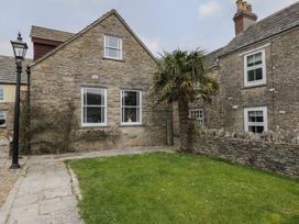 A stone house with windows a grass lawn a palm tree and a stone wall at The Old Haberdashery in Swanage