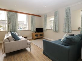 A living room with two sofas a wooden TV stand and windows with patterned curtains at The Old Haberdashery in Swanage