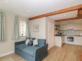 A living room with a blue sofa and patterned curtains next to a kitchen with white cabinets at The Old Haberdashery in Swanage