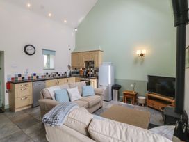 A living room with a kitchen area featuring a clock and a sofa at No 1 The Granary in Capel Coch near Llannerch-Y-Medd