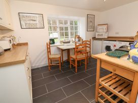 A kitchen with wooden chairs and table a microwave washing machine and a wooden trolley at The Cottage in Halkyn near Holywell
