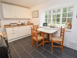 A kitchen with white cabinets a wooden table and chairs and a large window showing a garden at The Cottage in Halkyn near Holywell