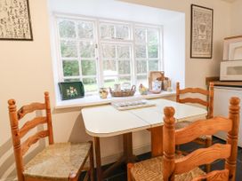 A dining area with a rectangular table and four wooden chairs next to a window with decorative items on the windowsill at The Cottage in Halkyn near Holywell