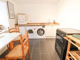 A kitchen with wooden chairs a white table a washing machine a dryer a microwave an oven and white cabinets at The Cottage in Halkyn near Holywell