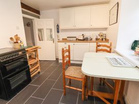 A kitchen with a black oven wooden chairs a white table white cabinets and a wooden counter at The Cottage in Halkyn near Holywell