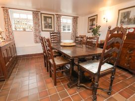A dining room with a wooden table and chairs with a bowl on the table and floral curtains at The Cottage in Halkyn near Holywell