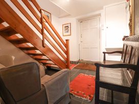 A hallway with a wooden staircase a fabric armchair a wooden bench and red rugs at The Cottage in Halkyn near Holywell