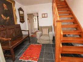 A hallway with a wooden bench a beige armchair a red rug and wooden stairs at The Cottage in Halkyn near Holywell