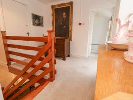 A hallway with a wooden railing a large framed portrait a chest of drawers and decorative pottery on a wooden surface at The Cottage in Halkyn near Holywell