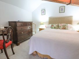 A bedroom with a bed with floral pillows side tables with lamps a wooden chest of drawers and a chair at The Cottage in Halkyn near Holywell