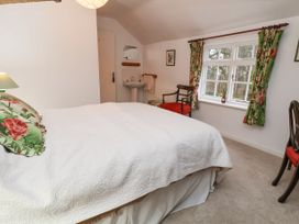 A bedroom with a bed white bedspread floral pillows a window with floral curtains two chairs and a sink at The Cottage in Halkyn near Holywell