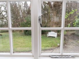 A garden with green grass a white bench and trees viewed through a window at The Cottage in Halkyn near Holywell