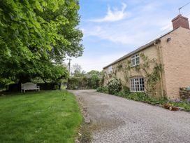 A gravel driveway next to a stone house with climbing plants and a green lawn with a white bench under a tree at The Cottage Halkyn near Holywell