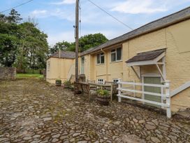 An outdoor area with a cobblestone ground wooden benches and potted plants next to a yellow brick building with windows and a green door at The Cottage Halkyn near Holywell