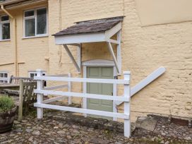 A green door below white awning with white fence and wooden chairs outside at The Cottage in Halkyn near Holywell
