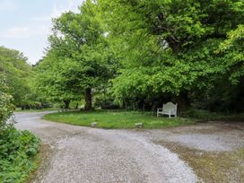A gravel driveway curving around a grassy area with large trees and a white bench at The Cottage in Halkyn near Holywell