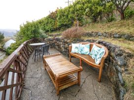 An outdoor patio with a wooden bench with cushions a wooden coffee table and a round table with two chairs at Y Stabal in Llanddoged near Llanrwst