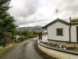 A paved driveway beside a house with a small garden and trees with hills in the background at Y Stabal in Llanddoged near Llanrwst
