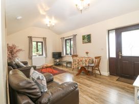 A living room with leather sofas a wooden table a small dining table with chairs and windows with curtains at Y Stabal Llanddoged near Llanrwst