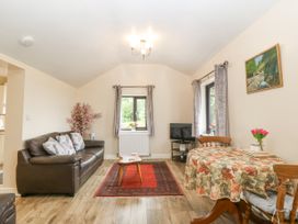 A living room with a brown sofa, a red rug, a wooden coffee table, a TV on a stand, a dining table with a floral tablecloth and chairs at Y Stabal in Llanddoged near Llanrwst