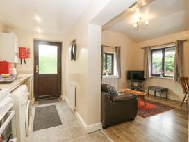 A kitchen area with white cabinets and appliances next to a living room with a leather sofa a TV and wooden furniture at Y Stabal in Llanddoged near Llanrwst