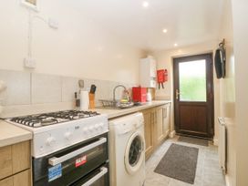 A kitchen with a stove, washing machine, countertop with sink, cabinets, a door, and kitchen utensils at Y Stabal in Llanddoged near Llanrwst