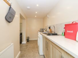 A narrow kitchen with wooden cabinets a countertop with a sink a red bread box and kitchen utensils at Y Stabal in Llanddoged near Llanrwst