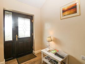 An entrance hallway with a dark wood door with decorative glass panels a white table with a lamp and brochures and a framed picture on the wall at Y Stabal in Llanddoged near Llanrwst