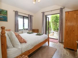 A bedroom with a wooden bed and wardrobe two windows with curtains and a door leading outside at Y Stabal in Llanddoged near Llanrwst