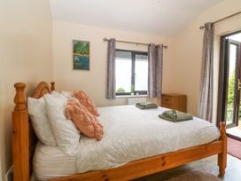 A bedroom with a wooden bed and pillows towels on the bed a window with curtains wooden dresser and glass door at Y Stabal in Llanddoged near Llanrwst