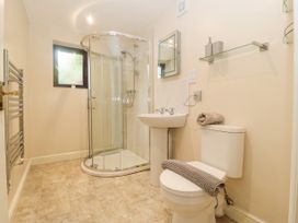 A bathroom with a corner shower, pedestal sink, toilet, towel rail, and glass shelf with soap dispensers at Y Stabal in Llanddoged near Llanrwst